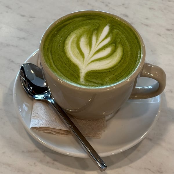 A vibrant green matcha latte with delicate latte art in a beige mug on a white saucer.
