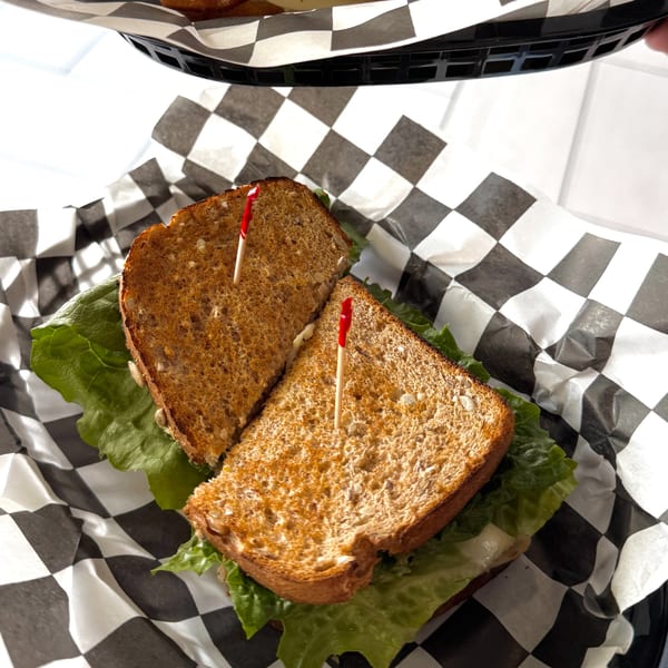 Toasted sandwich with lettuce and toothpicks, served in a basket with checkered paper at Sunny Cafe.