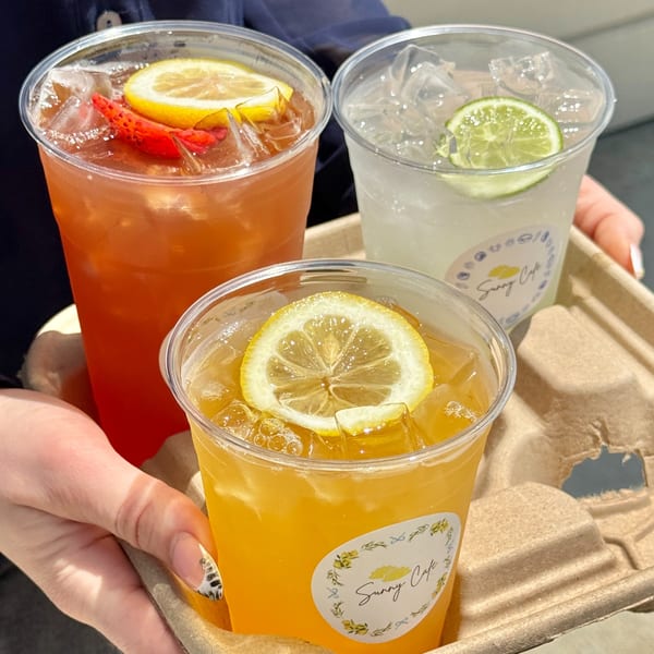 Three Sunny Cafe iced drinks, two with lemon and one with lime, in a cardboard carrier.