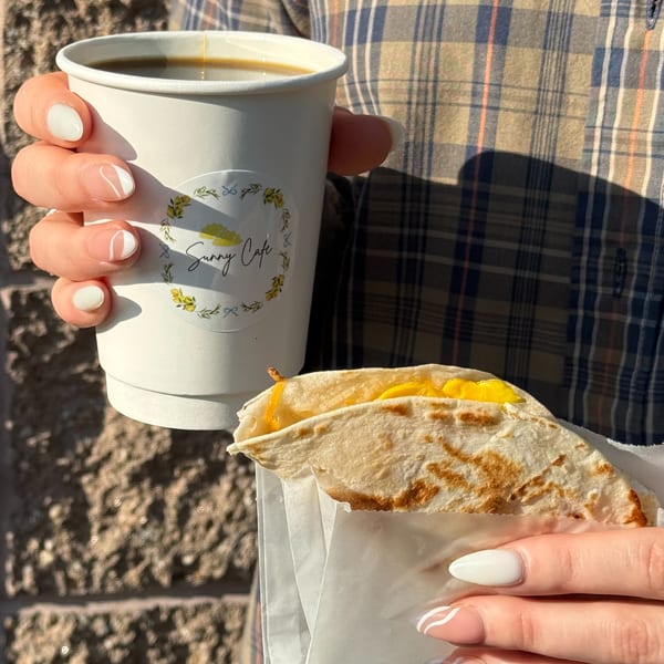 Hands holding a Sunny Cafe coffee cup and a breakfast quesadilla with melted cheese.