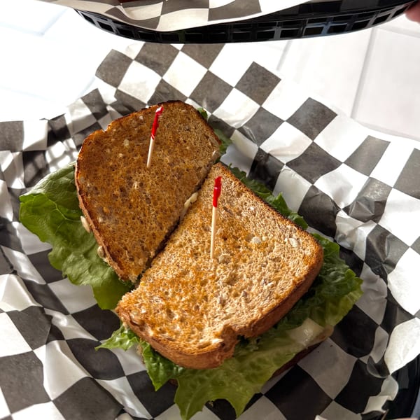Toasted sandwich with lettuce and red toothpicks, served in a basket with checkered paper.