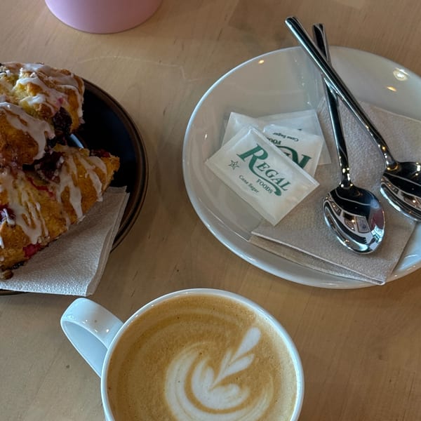 A latte with latte art, pastries, and sugar packets on a wooden table at Sunny Cafe.