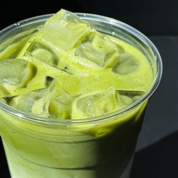 Close-up of an iced matcha latte with foam and ice cubes in a clear plastic cup.