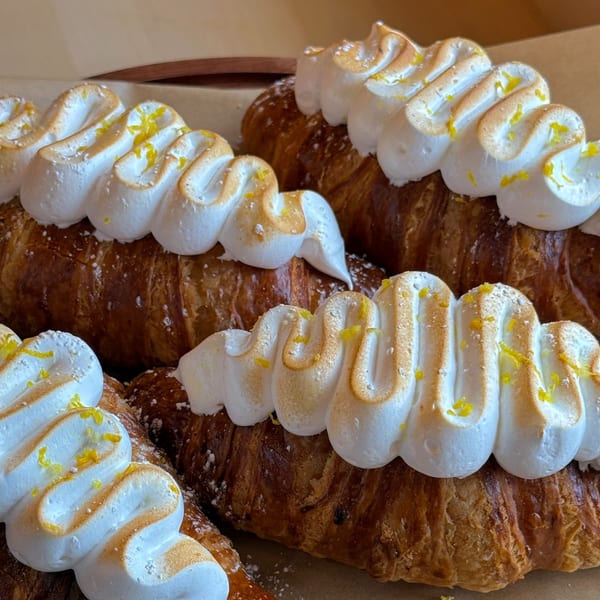Close-up of several golden-brown croissants topped with toasted meringue and lemon zest.