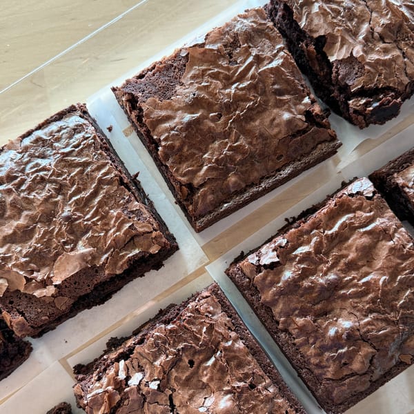 Close-up of several rich, fudgy brownies with crinkled tops, arranged on parchment paper.