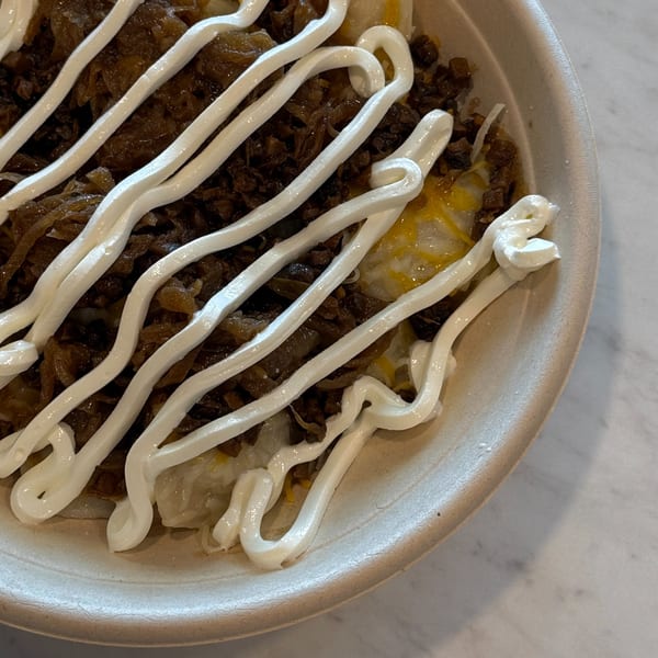 Close-up of a Sunny Cafe dish with meat, cheese, and white sauce in a bowl.