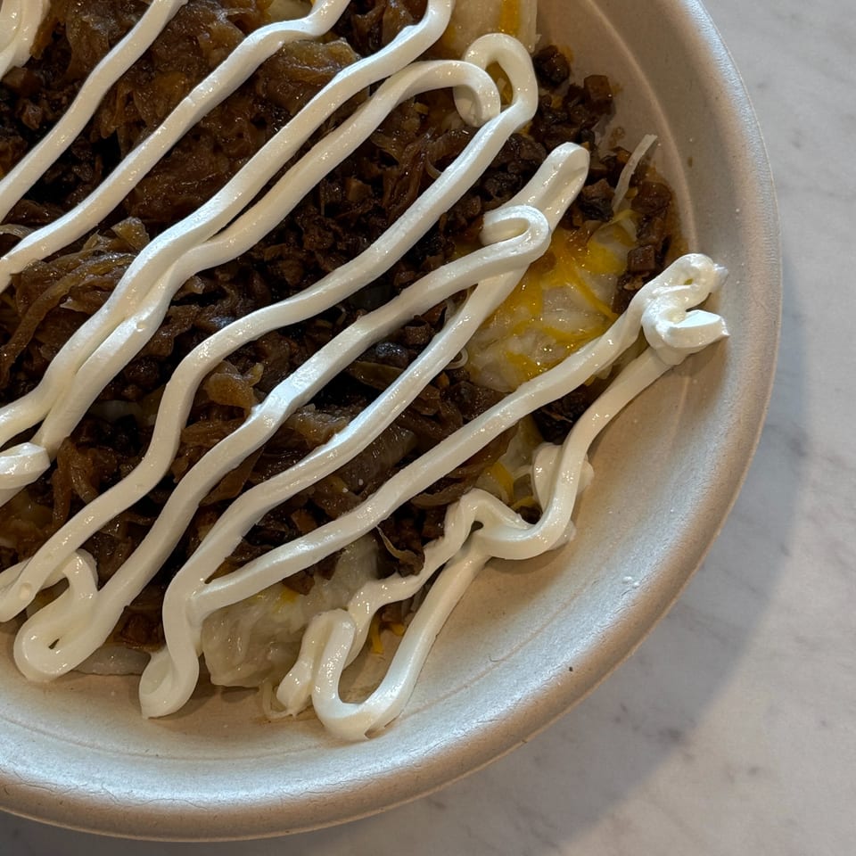 Close-up of a Sunny Cafe dish with meat, cheese, and white sauce in a bowl.