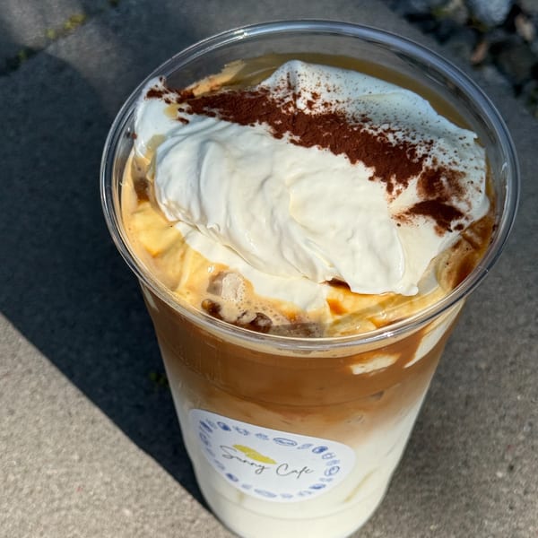 Iced coffee with whipped cream and cocoa powder, featuring the Sunny Cafe logo.