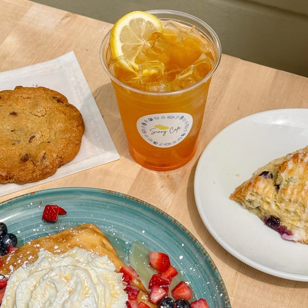 Sunny Cafe iced tea, cookie, scone, and crepe with whipped cream and berries on a wooden table.