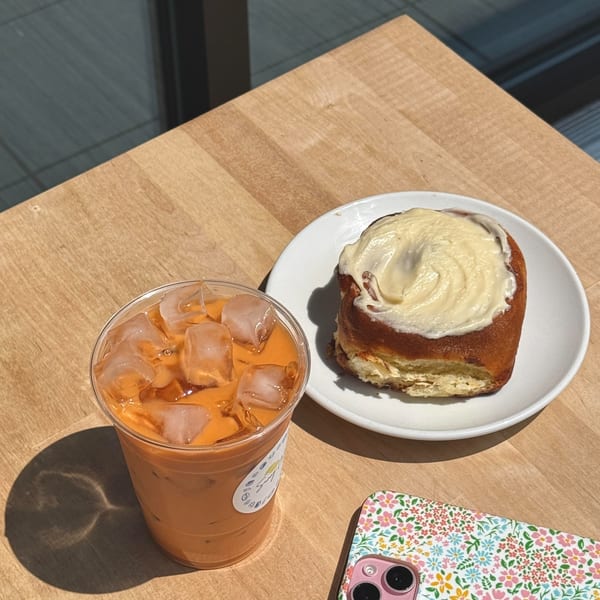 Iced Thai tea and a cinnamon roll with cream cheese frosting on a wooden table at Sunny Cafe.