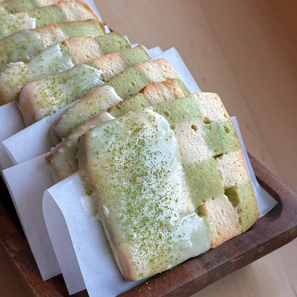 Rows of checkerboard matcha and plain bread slices, some topped with white glaze and green powder.