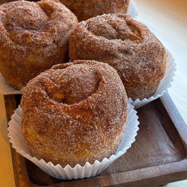 Four cinnamon sugar buns in white paper liners on a wooden tray from Sunny Cafe.