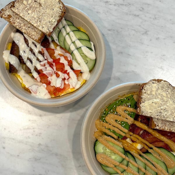 Two breakfast bowls from Sunny Cafe, one with white sauce, the other with orange sauce, on a marble table.