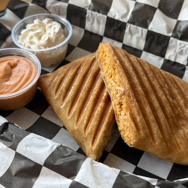 Grilled cheese panini with two dipping sauces in a black and white checkered basket.