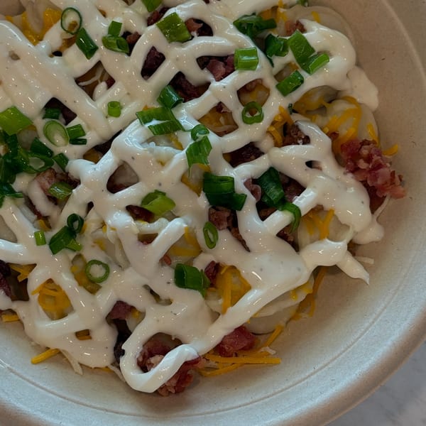 A close-up of Sunny Cafe's loaded potato dish with sour cream, bacon, cheese, and green onions.